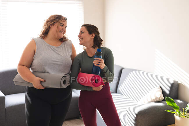 Lesbian couples practicing yoga, holding yoga mats smiling. domestic lifestyle, spending free time at home. — Stock Photo