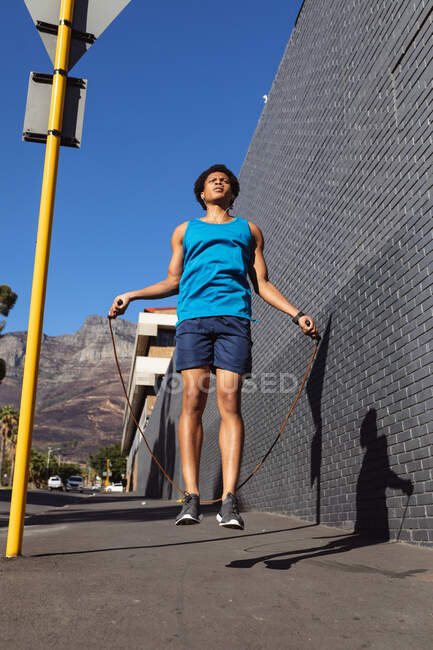 Ajuste hombre afroamericano ejercicio en la ciudad saltando con saltar la cuerda en la calle. fitness y estilo de vida urbano activo al aire libre. - foto de stock