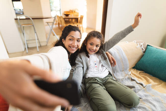 Misto razza madre e figlia seduta sul divano facendo facce divertenti, prendendo selfie. stile di vita domestico e trascorrere del tempo di qualità a casa. — Foto stock