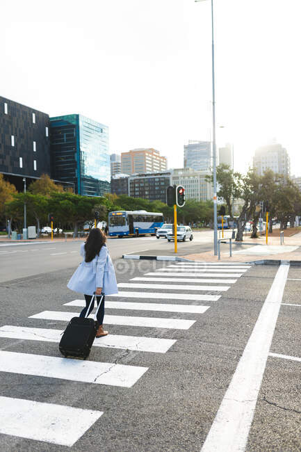 Азиатка переходит дорогу с чемоданом. независимая молодая женщина в городе. — стоковое фото