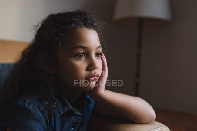 Portrait de fille ennuyée mixte assis sur le canapé dans le salon. style de vie domestique et passer du temps de qualité à la maison. — Photo de stock