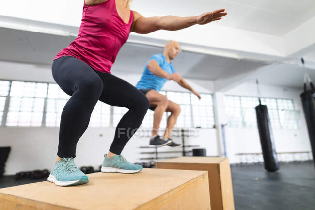 Кавказький чоловік і жінка тренуються в спортзалі, стрибаючи на коробках. міцність і пристосованість перехресна підготовка до боксу. — стокове фото