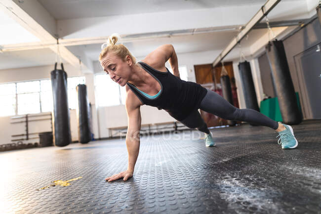 Strong caucasian woman exercising at gym, doing push-ups using one hand. strength and fitness cross training for boxing. — Stock Photo