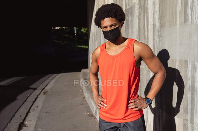 Portrait of fit african american man exercising in city wearing face mask. fitness and active urban outdoor lifestyle during coronavirus covid 19 pandemic. — Stock Photo