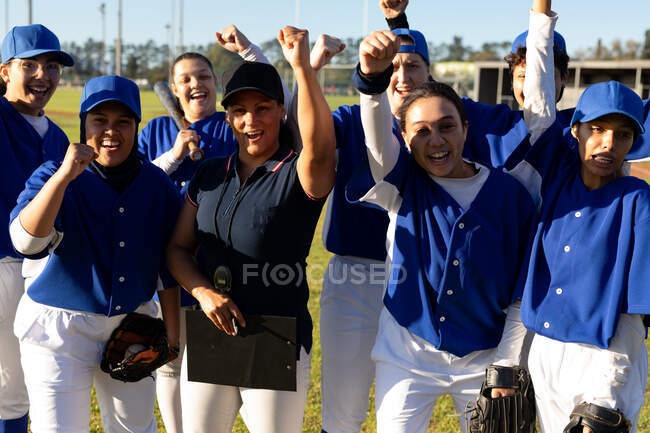 Grupo diverso de jogadoras felizes de beisebol e treinadoras comemorando no campo de beisebol após o jogo. time de beisebol feminino, treinamento esportivo, união e compromisso. — Fotografia de Stock