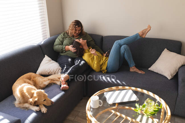 Feliz casal lésbico abraçando e sentado no sofá com o cão. estilo de vida doméstico, passar o tempo livre em casa. — Fotografia de Stock