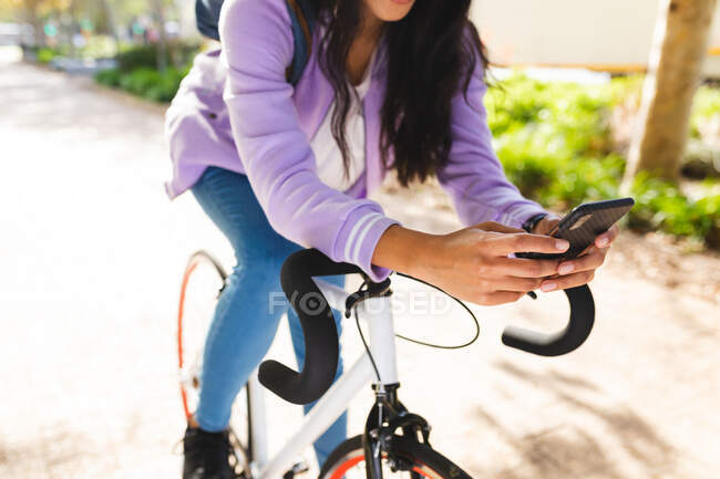 Mulher andando de bicicleta e usando smartphone no parque ensolarado. jovem independente para fora e sobre na cidade. — Fotografia de Stock