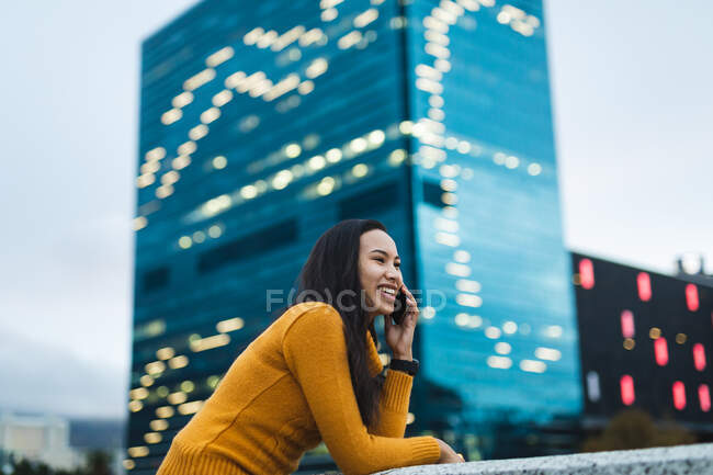 Азиатка, использующая смартфон и улыбающаяся на улице. независимая молодая женщина в городе. — стоковое фото