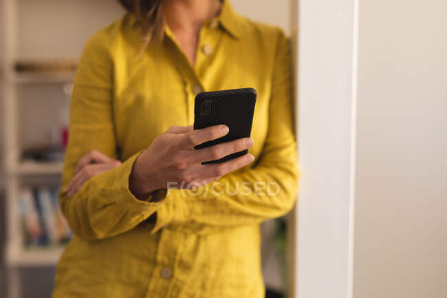 Femme portant une chemise jaune et utilisant un smartphone. mode de vie domestique, passer du temps libre à la maison. — Photo de stock