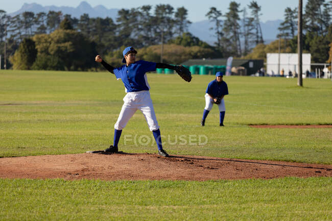 Mixed race female baseball pitcher on sunny baseball field throwing ball during game. female baseball team, sports training and game tactics. — Stock Photo