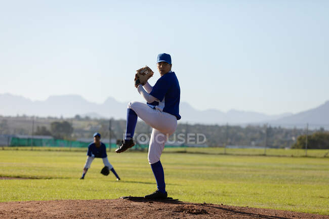 Mixed race female baseball pitcher on sunny baseball field preparing to throw ball during game. female baseball team, sports training and game tactics. — Stock Photo