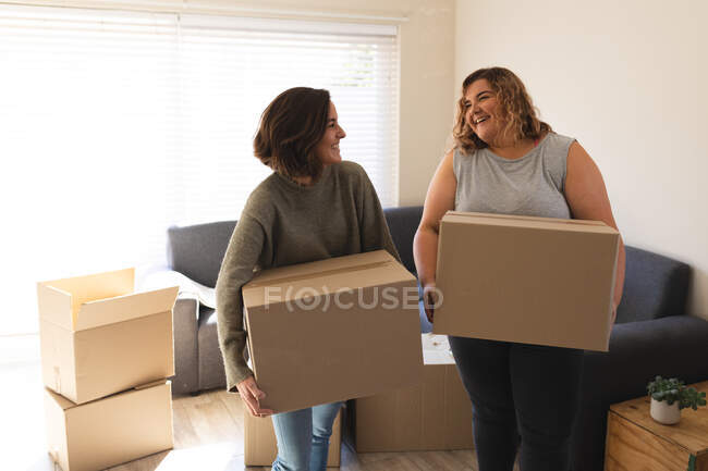 Lesbian couple smiling and holding boxes during moving house. domestic lifestyle, spending free time at home. — Stock Photo