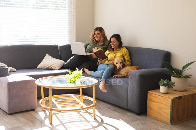 Casal de lésbicas usando laptop e sentado no sofá com o cão. estilo de vida doméstico, passar o tempo livre em casa. — Fotografia de Stock
