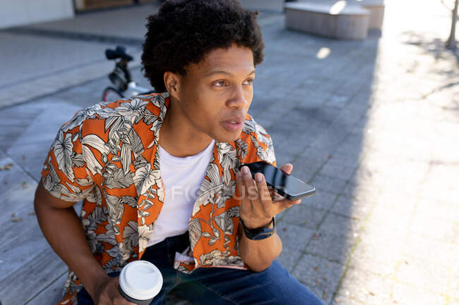 Homme afro-américain en ville assis et utilisant un smartphone. nomade numérique en déplacement, en déplacement dans la ville. — Photo de stock