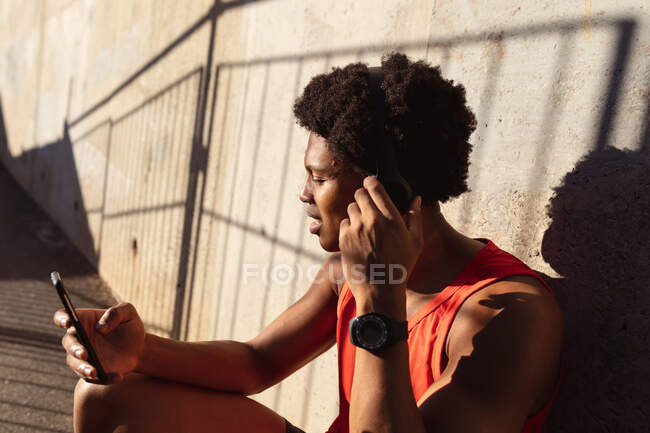 Fit afrikanisch-amerikanischer Mann, der in der Stadt mit dem Smartphone auf der Straße trainiert. Fitness und aktiver urbaner Lebensstil im Freien. — Stockfoto