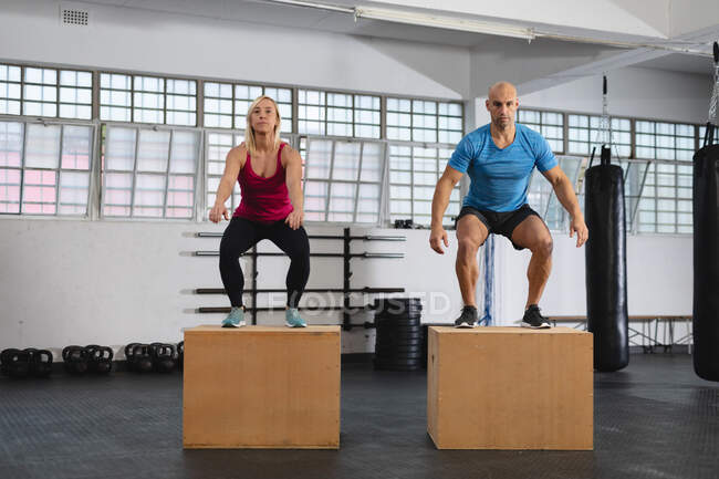 Caucásico hombre y mujer haciendo ejercicio en el gimnasio, saltando en cajas. entrenamiento cruzado de fuerza y fitness para boxeo. - foto de stock