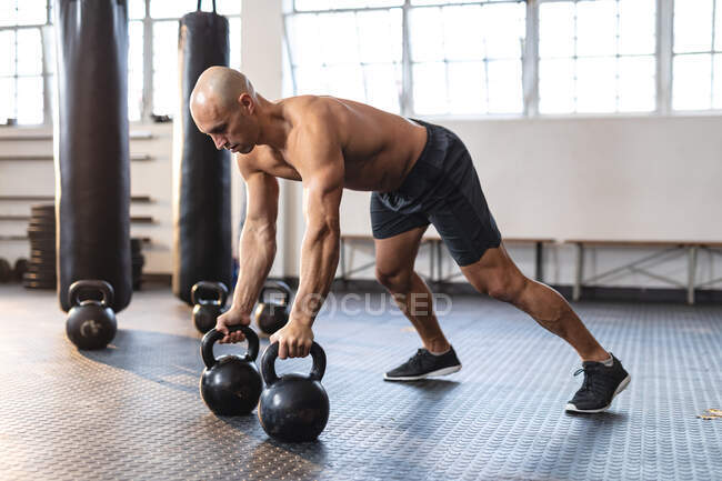 Hombre caucásico haciendo ejercicio en el gimnasio, haciendo flexiones usando pesas. entrenamiento cruzado de fuerza y fitness para boxeo. - foto de stock
