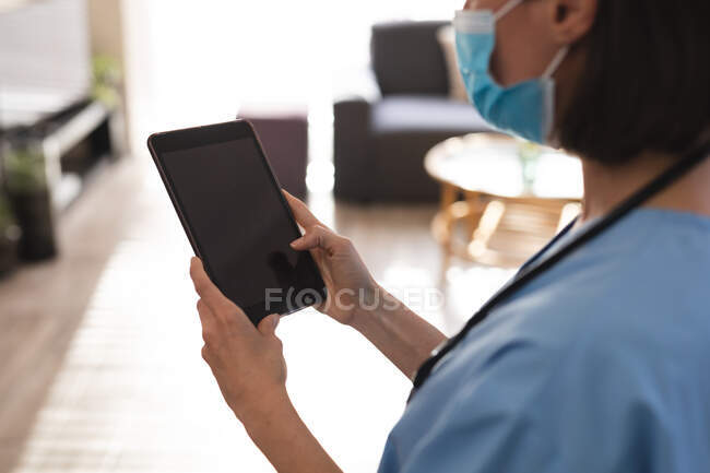 Médecin féminin caucasien portant un masque facial et utilisant une tablette. services médicaux et de santé pendant une pandémie de coronavirus covid 19. — Photo de stock
