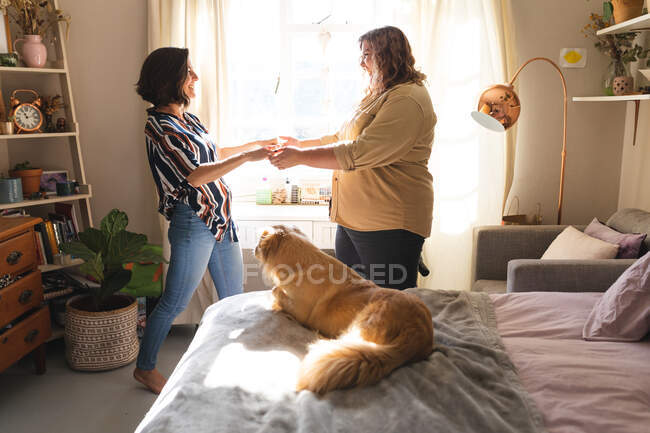 Glückliches lesbisches Paar, Händchen haltend und lächelnd im Schlafzimmer. häuslicher Lebensstil, Freizeit zu Hause verbringen. — Stockfoto