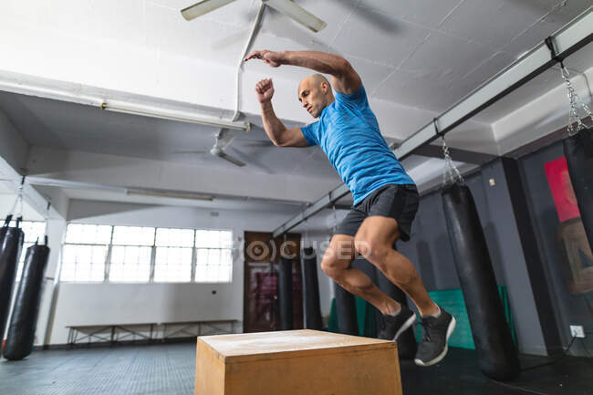 Белый мужчина тренируется в спортзале, прыгает на коробке. силовые и фитнес-кросс тренировки для бокса. — стоковое фото