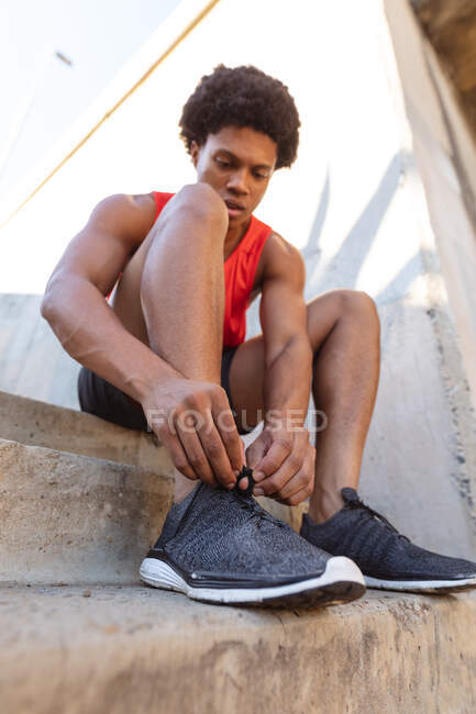 Fit african american man exercising in city tying shoes. fitness and active urban outdoor lifestyle. — Stock Photo