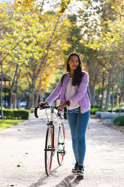 Asian woman wheeling bike in sunny park. independent young woman out and about in the city. — Stock Photo
