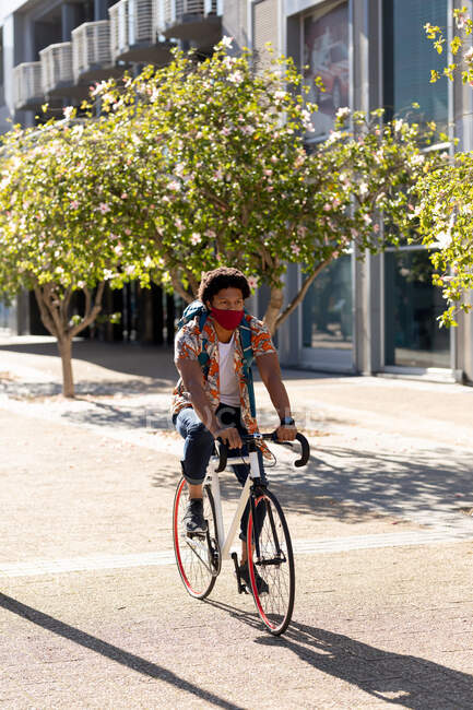Afroamerikaner in der Stadt mit Gesichtsmaske beim Radfahren. digitaler Nomade unterwegs, unterwegs in der Stadt während Coronavirus covid 19 Pandemie. — Stockfoto