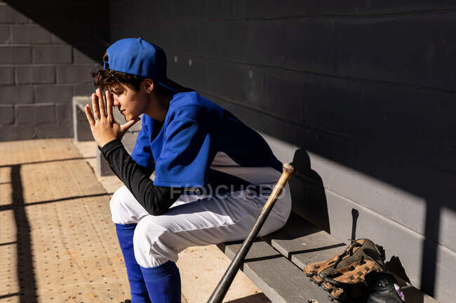 Mixed race female baseball player sitting on bench with bat preparing to play during game. female baseball team, sports training and game tactics. — Stock Photo