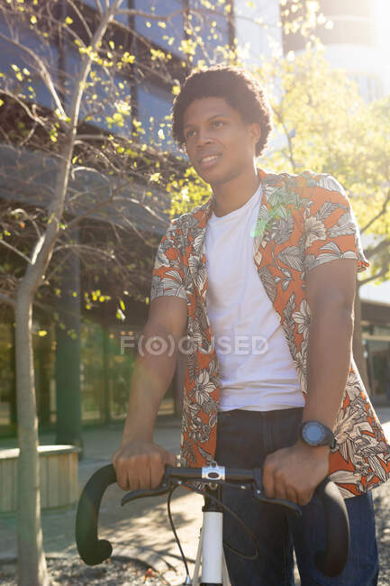Homem afro-americano na cidade sorrindo e segurando sua bicicleta. nômade digital em movimento, para fora e sobre na cidade. — Fotografia de Stock