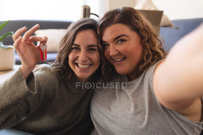 Retrato de pareja lesbiana moviendo casa sentada y sosteniendo la llave. estilo de vida doméstico, pasar tiempo libre en casa. - foto de stock