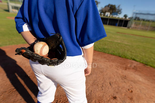 Мідсекктон жіночого бейсбольного пітчера на сонячному бейсбольному полі, що тримає м'яч в рукавичці під час гри. Жіноча бейсбольна команда, спортивна підготовка та ігрова тактика. — стокове фото