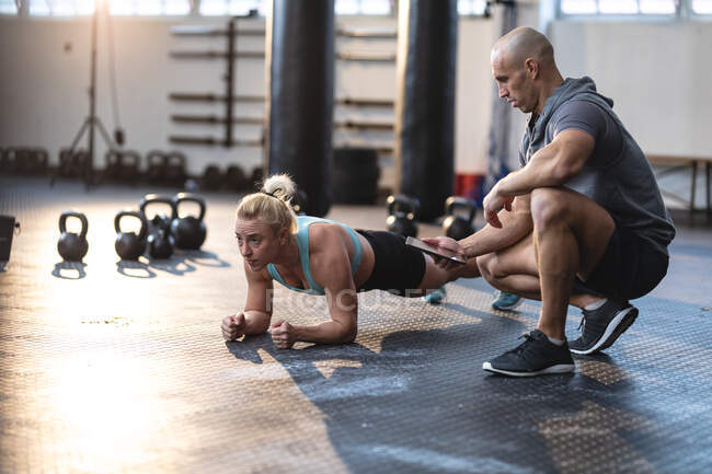 Treinador masculino caucasiano instruindo mulher se exercitando no ginásio, fazendo prancha. treinamento cruzado de força e aptidão para boxe. — Fotografia de Stock