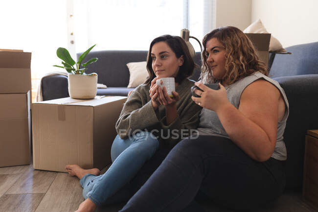 Pareja lesbiana mudándose casa sentado y bebiendo té. estilo de vida doméstico, pasar tiempo libre en casa. - foto de stock