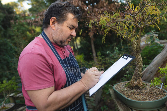 Profilo del giardiniere maschio caucasico che prende appunti al centro del giardino. specialista che lavora presso vivaio bonsai, attività orticola indipendente. — Foto stock