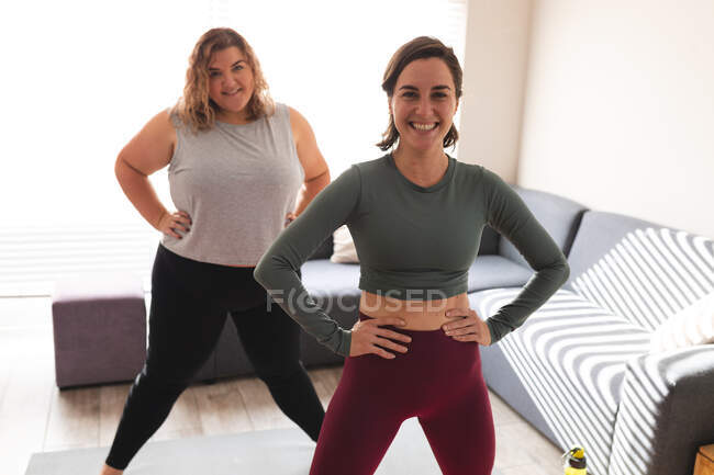 Ritratto di coppia lesbica che pratica yoga, guarda la macchina fotografica e sorride. stile di vita domestico, trascorrere il tempo libero a casa. — Foto stock