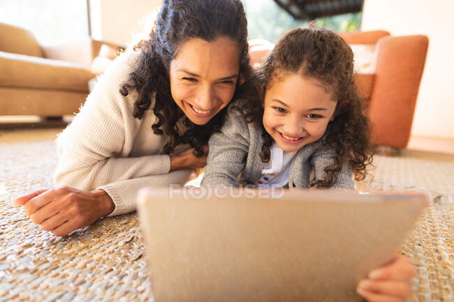 Mère et fille de race mixte allongées sur le tapis, en utilisant une tablette. style de vie domestique et passer du temps de qualité à la maison. — Photo de stock