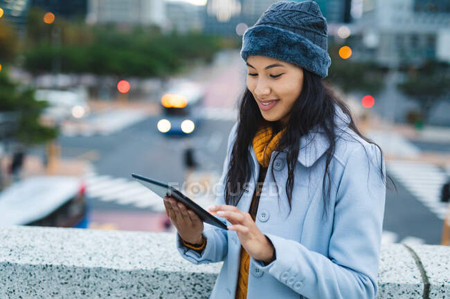 Азійка користується планшетом і посміхається на вулиці. Незалежна молода жінка у місті.. — стокове фото