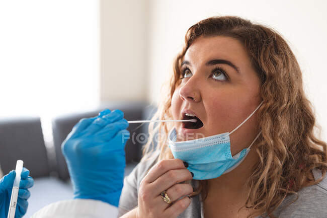 Female doctor wearing medical gloves taking swab test from female patient at home. medical and healthcare services home visiting during coronavirus covid 19 pandemic. — Stock Photo