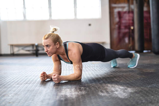 Mujer caucásica fuerte haciendo ejercicio en el gimnasio, haciendo tablón. entrenamiento cruzado de fuerza y fitness para boxeo. - foto de stock