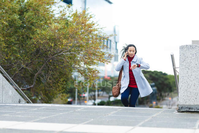 Asian woman using smartphone and checking smartwatch in the street. independent young woman out and about in the city. — Stock Photo