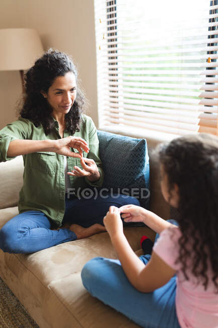 Mutter und Tochter einer gemischten Rasse sitzen auf dem Sofa, gestikulieren und spielen zusammen. Lebensstil und hochwertige Zeit zu Hause verbringen. — Stockfoto