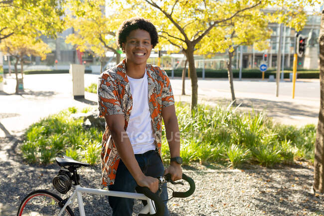 Retrato do homem afro-americano na cidade sorrindo e segurando sua bicicleta. nômade digital em movimento, para fora e sobre na cidade. — Fotografia de Stock