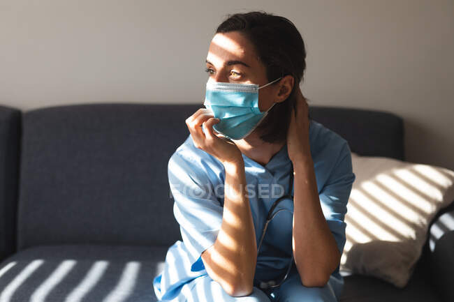 Caucasian female doctor wearing face mask and touching her neck. medical and healthcare services during coronavirus covid 19 pandemic. — Stock Photo