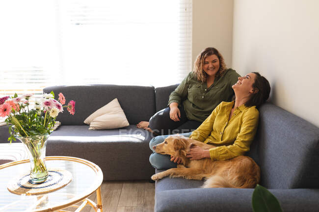 Lesbian couple smiling and sitting on couch with dog. domestic lifestyle, spending free time at home. — Stock Photo