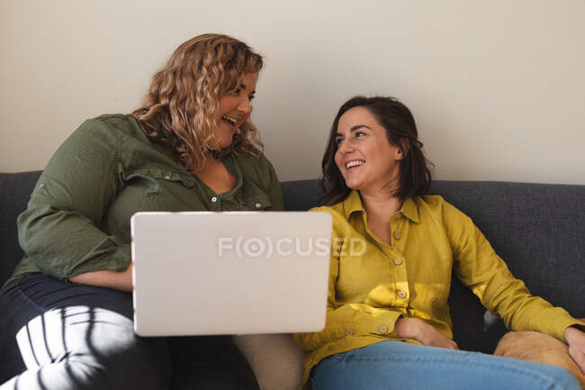 Lesbian couple using laptop and sitting on couch with dog. domestic lifestyle, spending free time at home. — Stock Photo