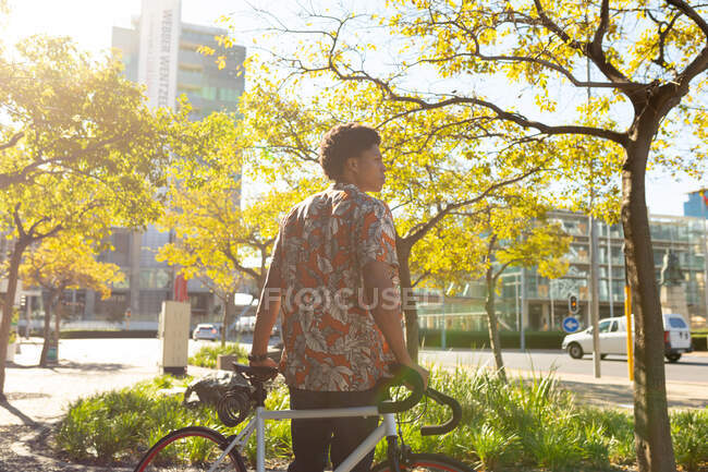Homem afro-americano na cidade olhando para longe e segurando sua bicicleta. nômade digital em movimento, para fora e sobre na cidade. — Fotografia de Stock