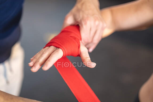 Entrenador masculino instruyendo a la mujer haciendo ejercicio en el gimnasio, envolviendo las manos con cinta adhesiva. entrenamiento cruzado de fuerza y fitness para boxeo. - foto de stock