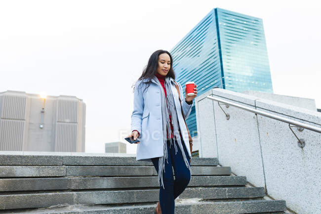 Mulher asiática segurando takeaway café e usando smartphone nas escadas. jovem independente para fora e sobre na cidade. — Fotografia de Stock