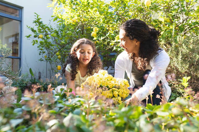 Mutter und Tochter einer gemischten Rasse pflanzen Blumen und unterhalten sich. Lebensstil und hochwertige Zeit zu Hause verbringen. — Stockfoto