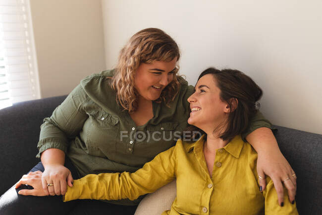 Lesbisches Paar lächelt, umarmt und sitzt auf der Couch. häuslicher Lebensstil, Freizeit zu Hause verbringen. — Stockfoto